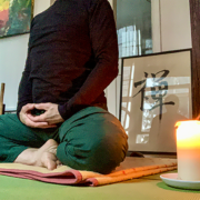 Person in Meditationshaltung mit kerze in einem raum